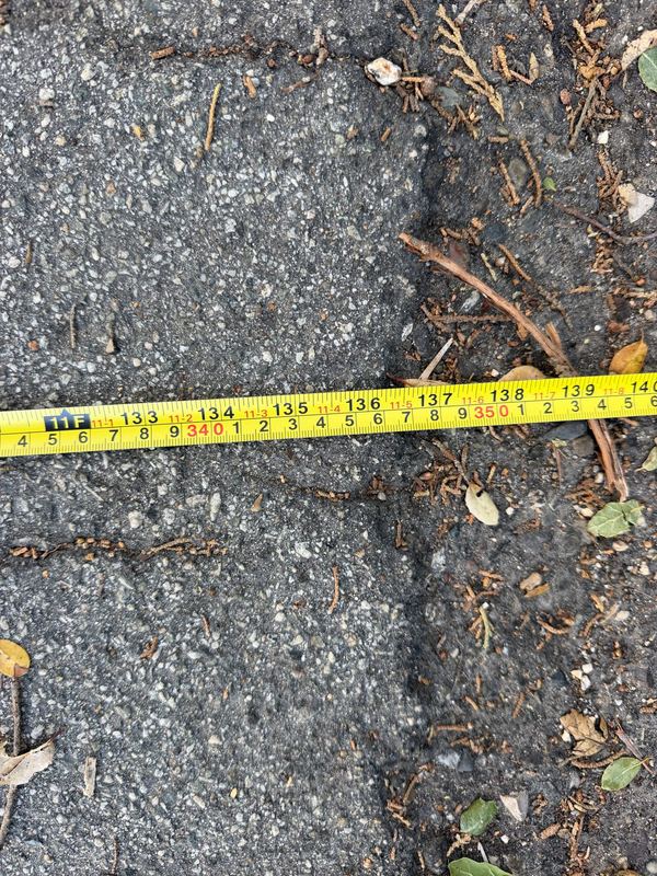 Close-up of the tape measure at the far pavement edge of Cima Linda Lane, reading 11 feet 6 inches.